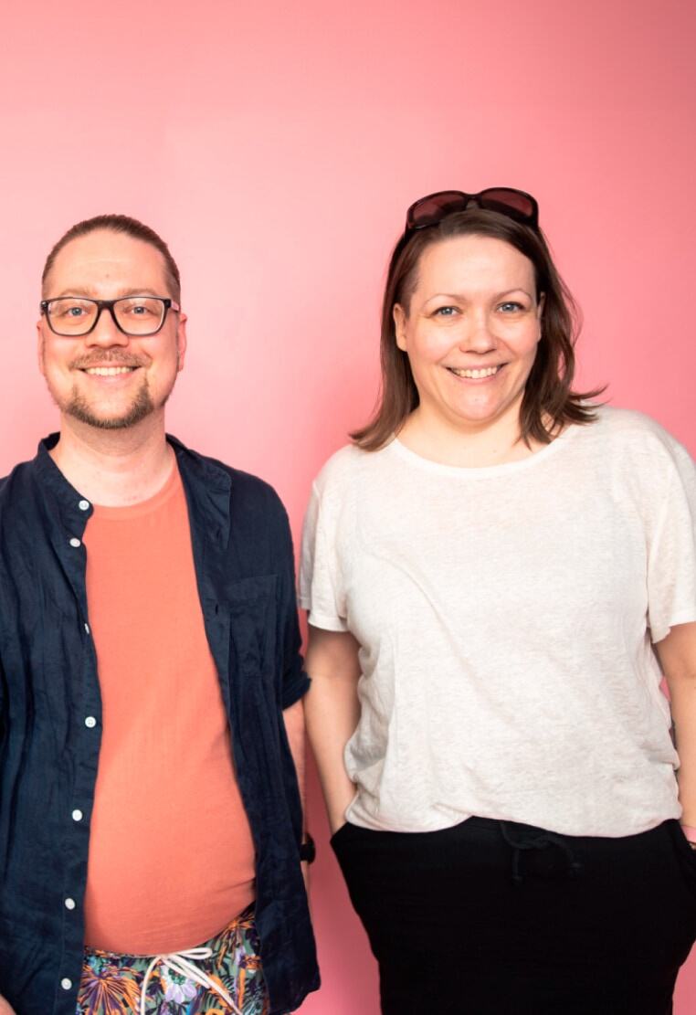Fraktio's workers Elsis and Mikko stand in a row smiling in front of a pink background