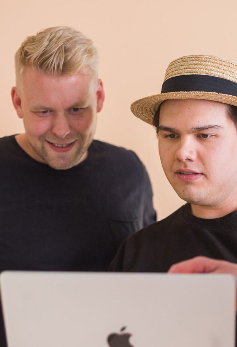  two developers looking at laptop screen in front of orange background.